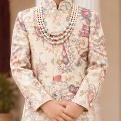 A child wearing a cream-colored traditional outfit with a colorful paisley pattern in pink, blue, and green, accessorized with a multi-strand pearl necklace.