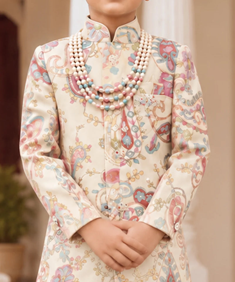 A child wearing a cream-colored traditional outfit with a colorful paisley pattern in pink, blue, and green, accessorized with a multi-strand pearl necklace.