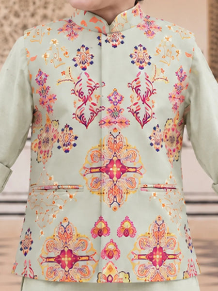A close-up of a person wearing a light sage green traditional jacket with a vibrant, multicolored floral and geometric pattern in pink, orange, yellow, and blue.