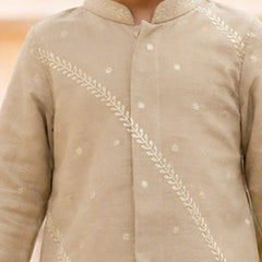 A close-up of a child wearing a light beige traditional long-sleeve kurta with white embroidered leaf and star motifs.