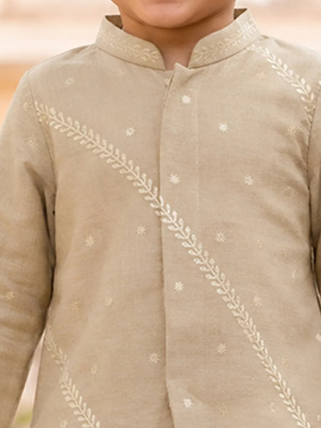 A close-up of a child wearing a light beige traditional long-sleeve kurta with white embroidered leaf and star motifs.