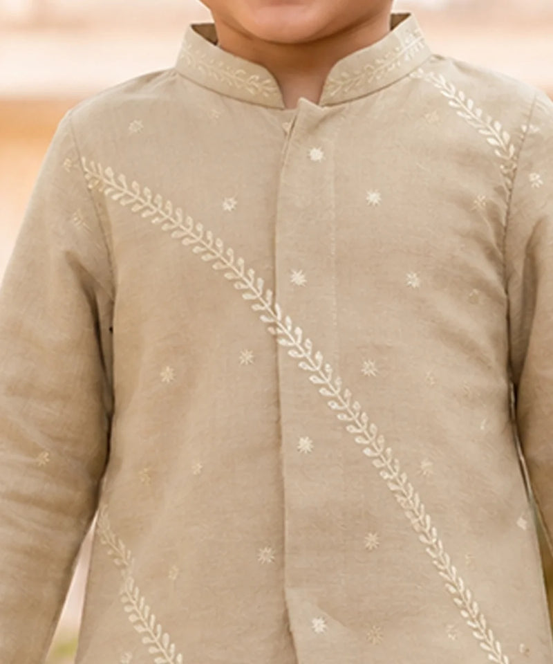 A close-up of a child wearing a light beige traditional long-sleeve kurta with white embroidered leaf and star motifs.