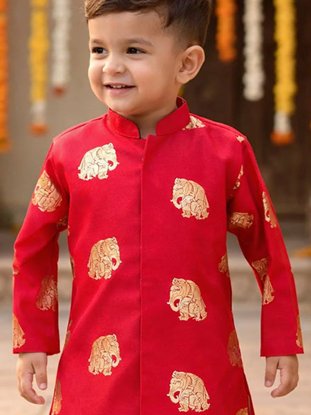 Child wearing a red traditional outfit with gold patterns, standing against a decorative background.