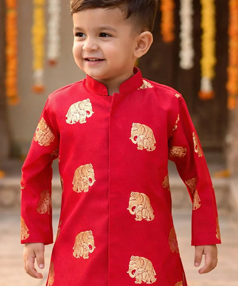 Child wearing a red traditional outfit with gold patterns, standing against a decorative background.