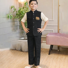 Child wearing a formal outfit with a vest and pants in a room with plants and a pink chair.