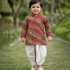 Child wearing a traditional outfit with a patterned shirt and white dhoti standing outdoors.
