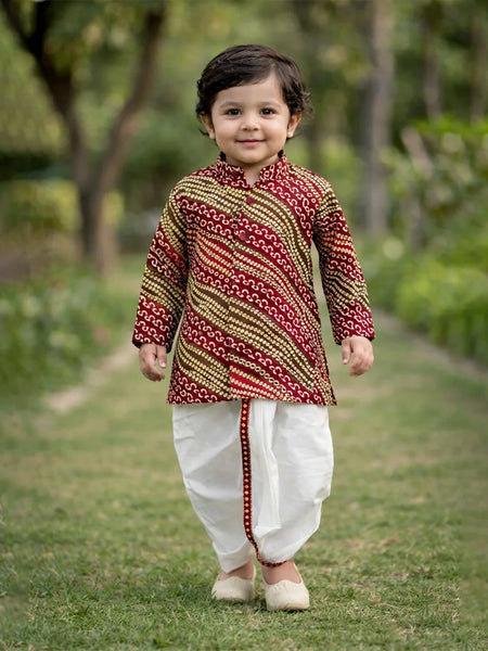 Child wearing a traditional outfit with a patterned shirt and white dhoti standing outdoors.
