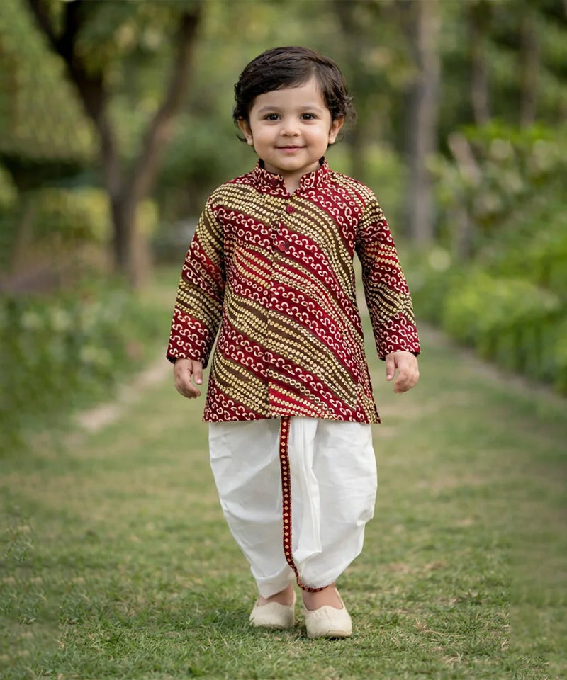 Child wearing a traditional outfit with a patterned shirt and white dhoti standing outdoors.