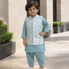 Child wearing a traditional outfit with a light blue vest and pants, standing outdoors.