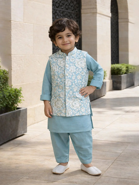 Child wearing a traditional outfit with a light blue vest and pants, standing outdoors.