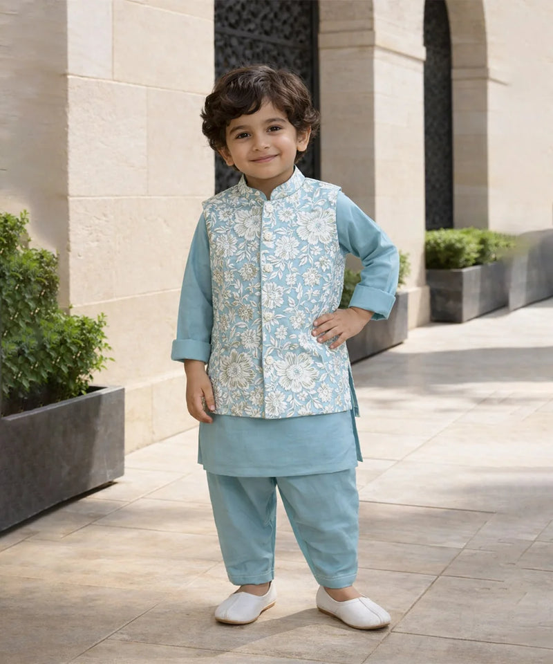 Child wearing a traditional outfit with a light blue vest and pants, standing outdoors.