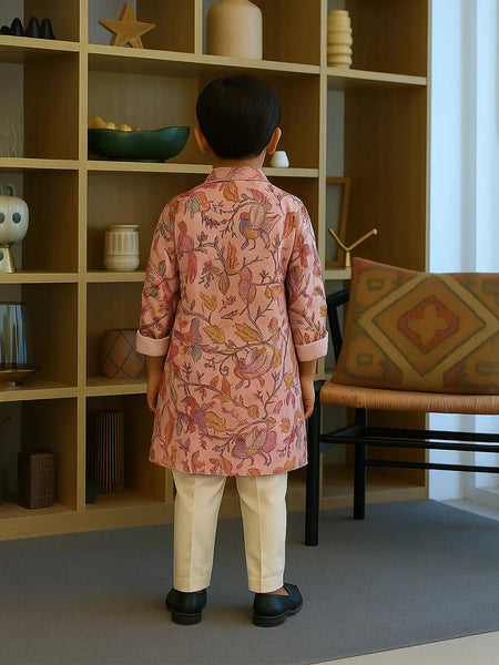 Child wearing a pink floral kurta standing in a room with a bookshelf and chair.