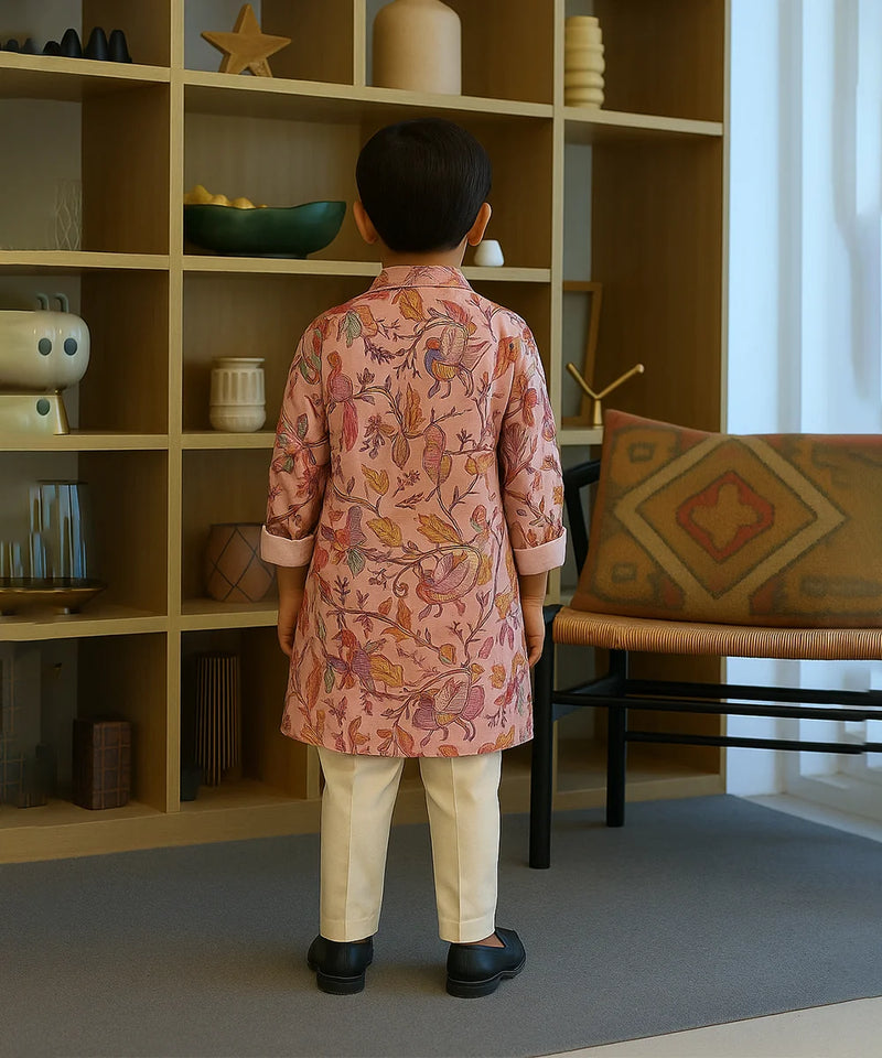 Child wearing a pink floral kurta standing in a room with a bookshelf and chair.