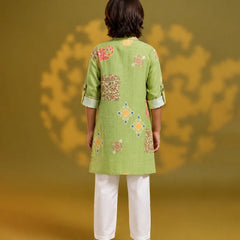 A model viewed from the back wearing a light green kurta with colorful floral and geometric embroidery, paired with white trousers, set against a warm yellow background with soft shadow details.