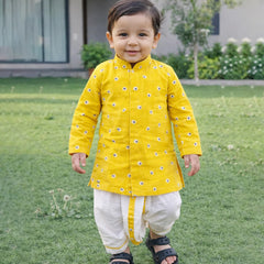 Child wearing a yellow traditional outfit with white pants standing on grass.