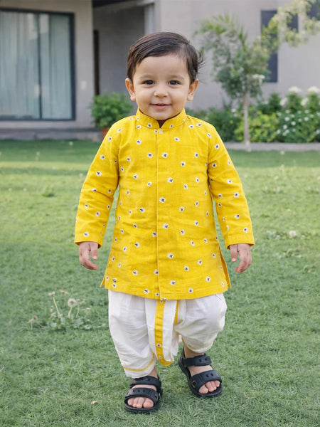 Child wearing a yellow traditional outfit with white pants standing on grass.