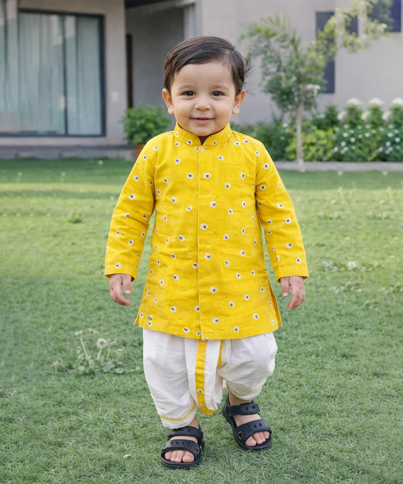Child wearing a yellow traditional outfit with white pants standing on grass.