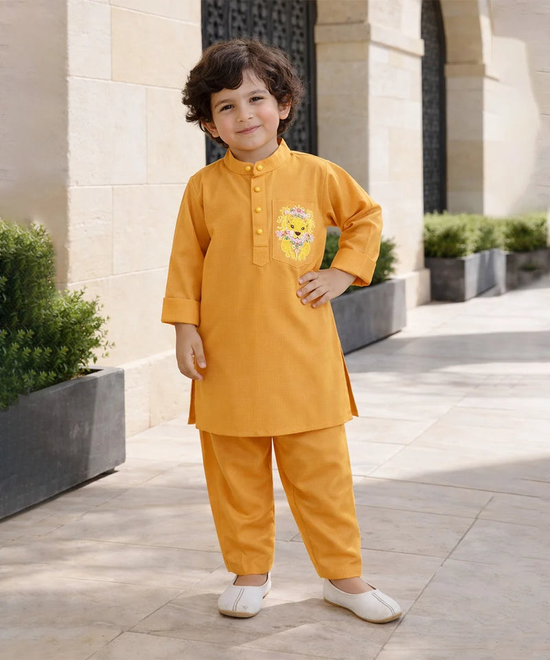 Child wearing a mustard yellow traditional outfit with a cartoon character, standing outdoors.