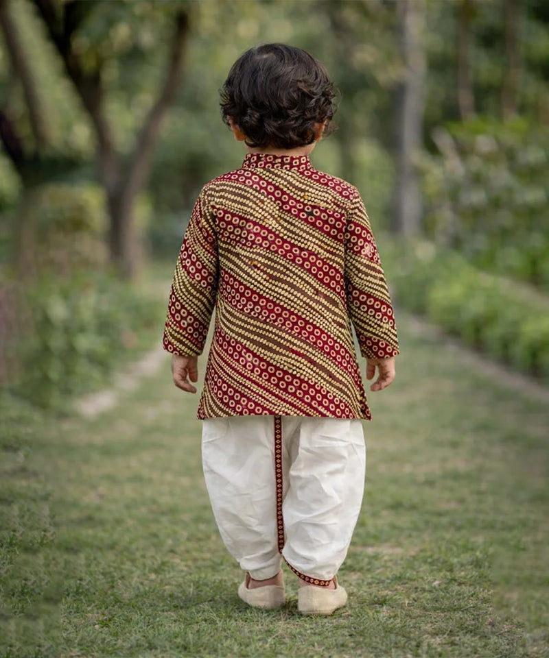 Child wearing a patterned kurta and white pants walking outdoors.