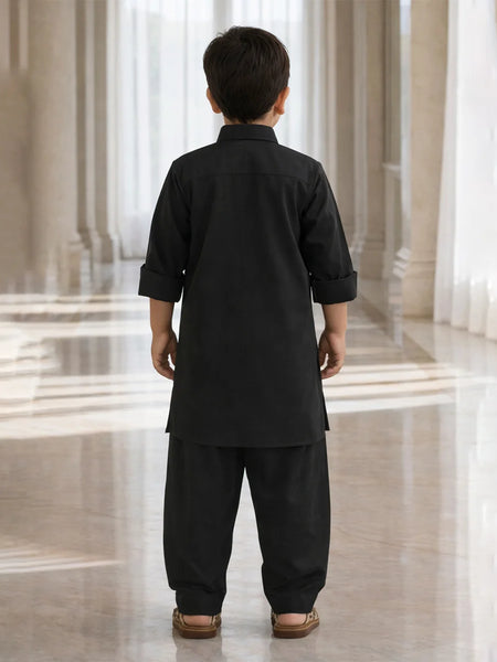 Child wearing a black traditional outfit standing in a marble hallway.