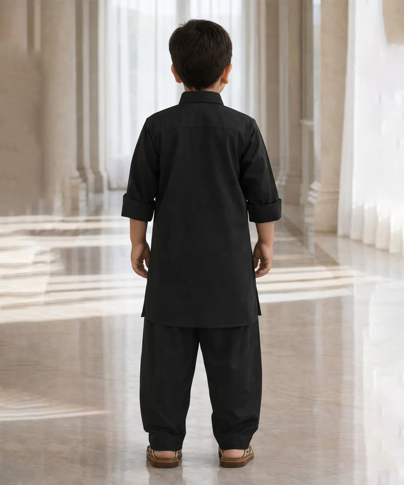 Child wearing a black traditional outfit standing in a marble hallway.