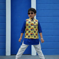 Child wearing a colorful vest over a blue kurta with white pants against a blue wall.