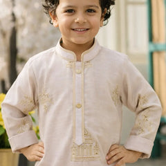 Child wearing a beige embroidered kurta with gold details, standing outdoors.