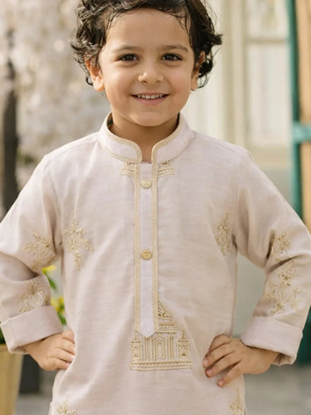 Child wearing a beige embroidered kurta with gold details, standing outdoors.