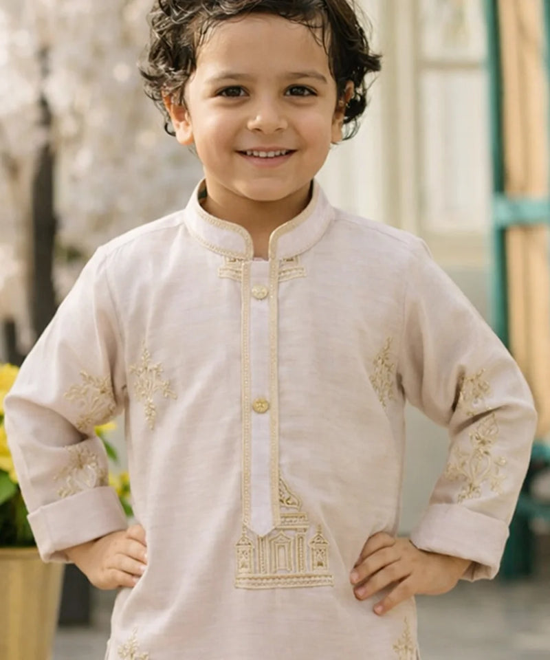 Child wearing a beige embroidered kurta with gold details, standing outdoors.