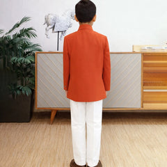 Person wearing an orange coat and white pants standing in a room with a plant and wooden cabinet.