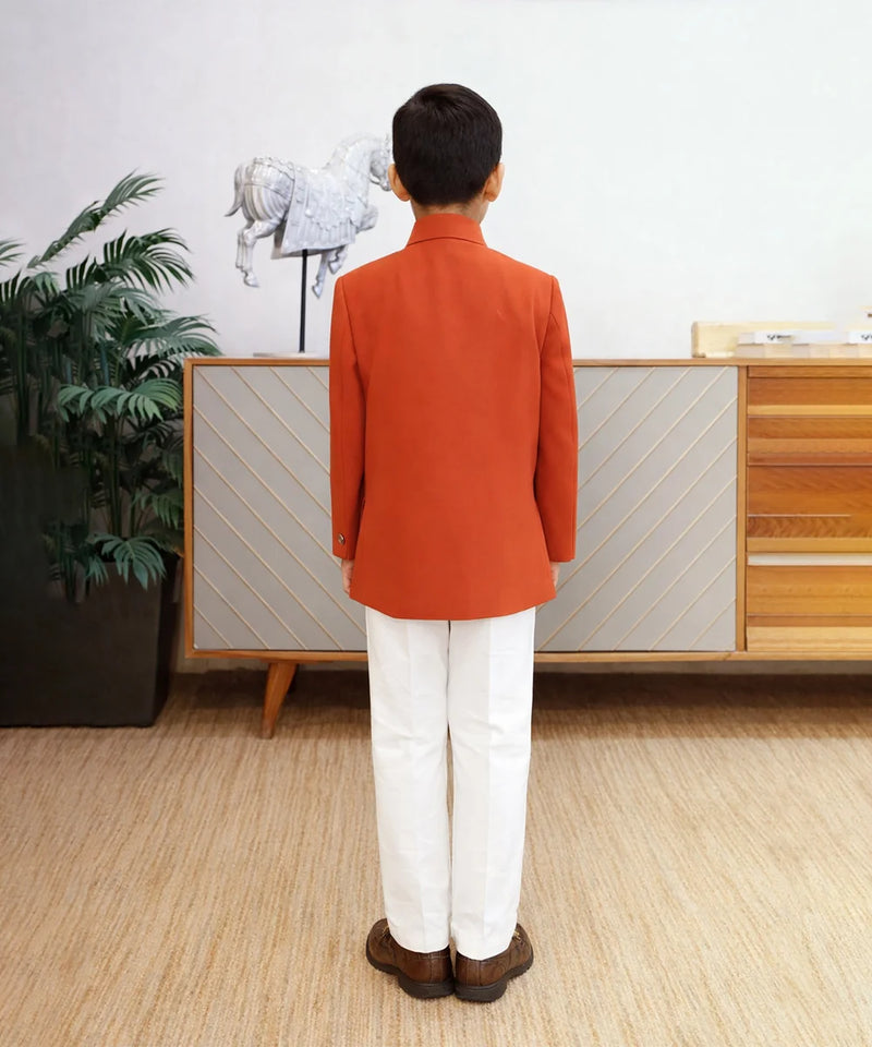 Person wearing an orange coat and white pants standing in a room with a plant and wooden cabinet.