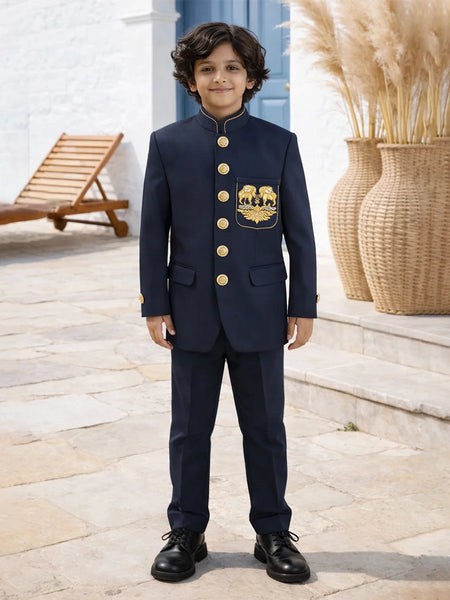 Young boy in a navy suit with gold buttons standing outdoors.