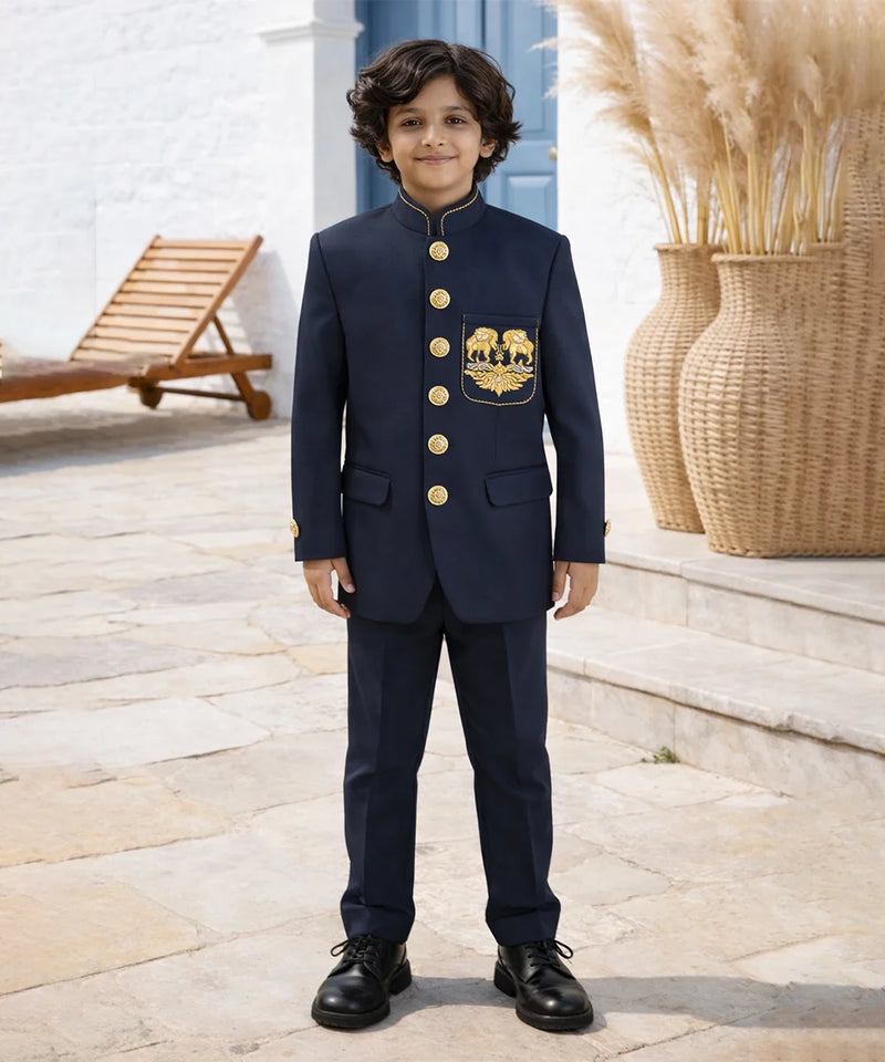 Young boy in a navy suit with gold buttons standing outdoors.
