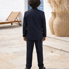 Person wearing a navy suit standing outdoors with a blue door and pampas grass in the background.