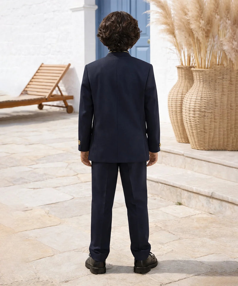 Person wearing a navy suit standing outdoors with a blue door and pampas grass in the background.