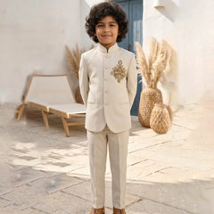 Child in a formal beige suit standing outdoors with decorative elements in the background