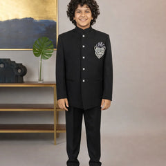 Child wearing a black formal suit with a decorative emblem, standing against a neutral background.