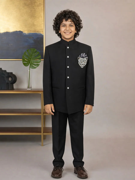 Child wearing a black formal suit with a decorative emblem, standing against a neutral background.