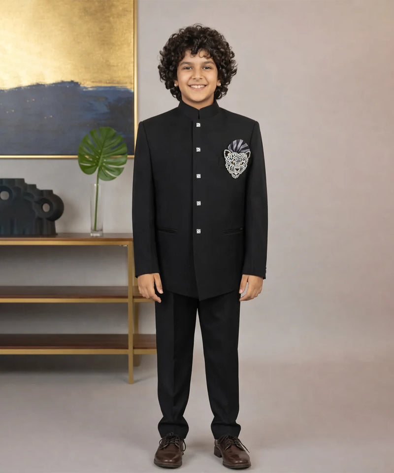 Child wearing a black formal suit with a decorative emblem, standing against a neutral background.