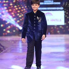 Young boy in a blue velvet jodhpuri  suit walking on a runway with colorful lights in the background