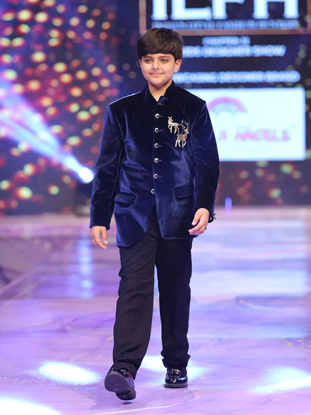 Young boy in a blue velvet jodhpuri  suit walking on a runway with colorful lights in the background