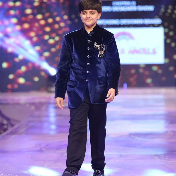 Young boy in a blue velvet jodhpuri  suit walking on a runway with colorful lights in the background