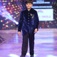 Young boy in a blue velvet jodhpuri  suit walking on a runway with colorful lights in the background