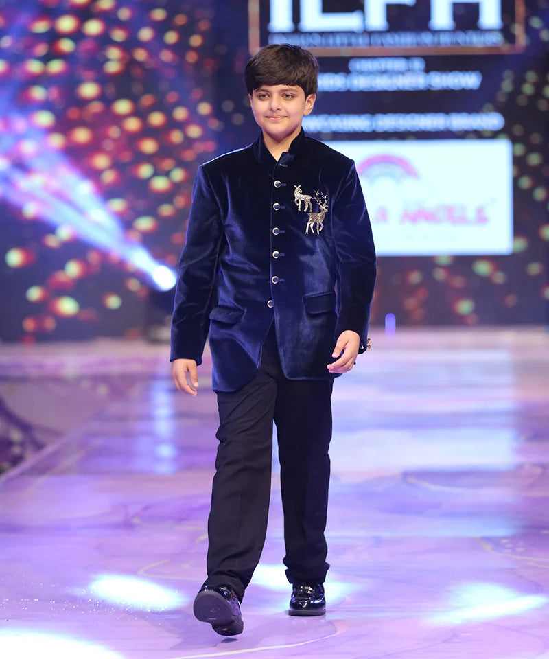 Young boy in a blue velvet jodhpuri  suit walking on a runway with colorful lights in the background