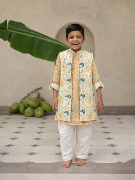 Child wearing a traditional outfit with a floral pattern in a room with a plant and fruit.