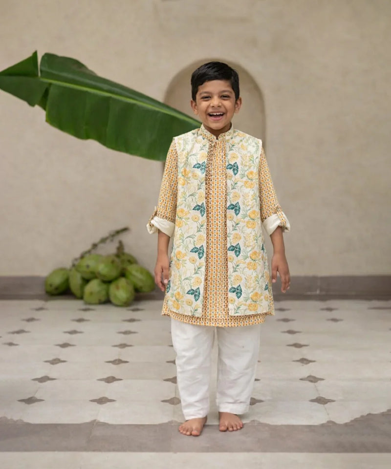 Child wearing a traditional outfit with a floral pattern in a room with a plant and fruit.