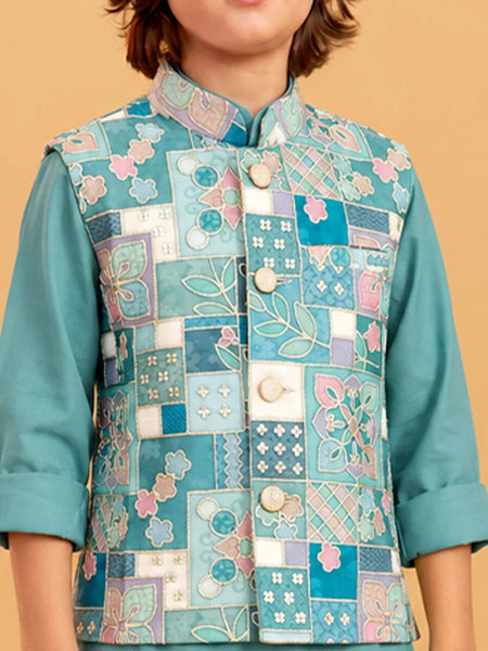 A child wearing a teal embroidered vest with a patchwork floral design over a matching teal long-sleeve shirt, set against a solid beige background.