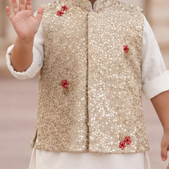 A child wearing a beige sequined vest with red floral embroidery over a white kurta, with one hand raised in a wave.