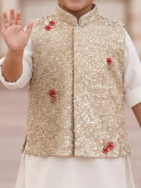A child wearing a beige sequined vest with red floral embroidery over a white kurta, with one hand raised in a wave.