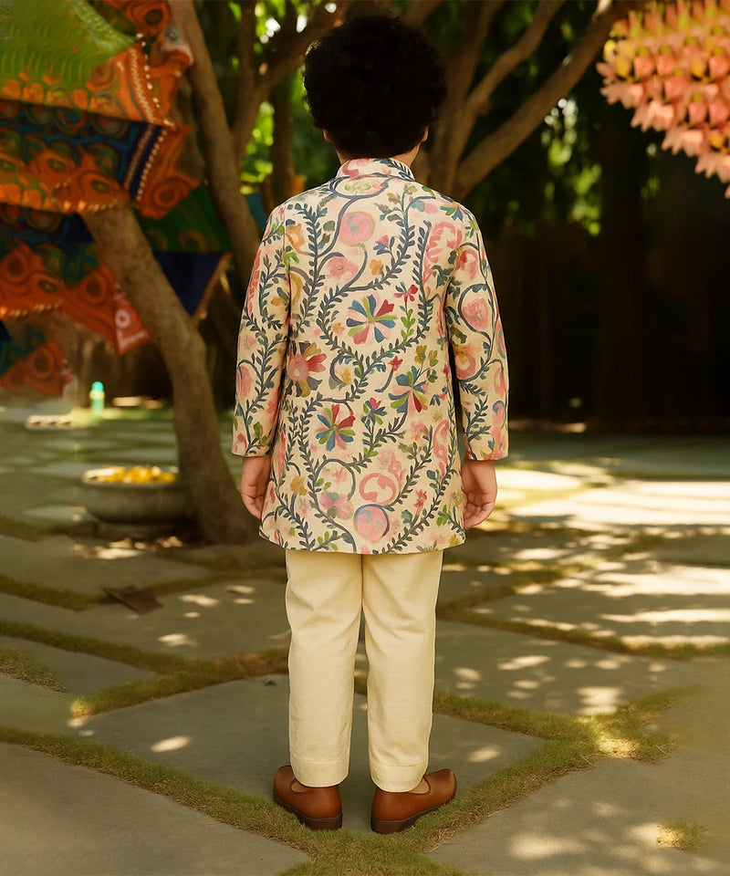Person wearing a floral embroidered jacket and beige pants in an outdoor setting with trees and decorations.